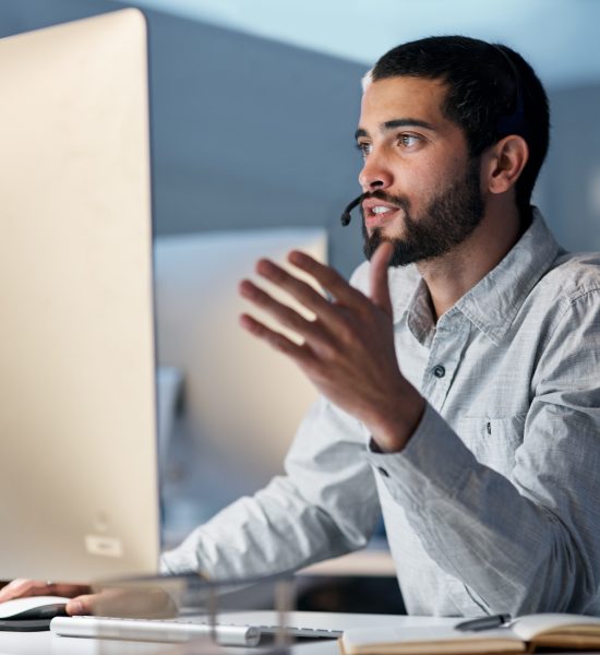 A man helping to an IT customer on the computer using a headset.