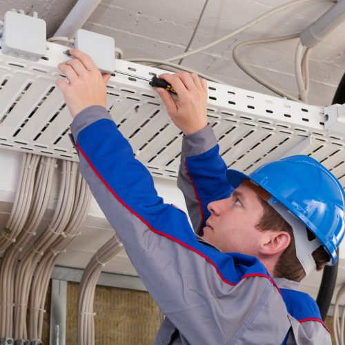 A technician installing networking equipment in a server room, focused on connecting cables and configuring devices.