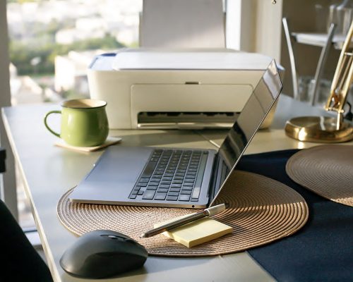 A printer and a laptop next to each other on an office desk.